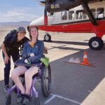 Woman in a wheelchair smiling under the wing of an airplane